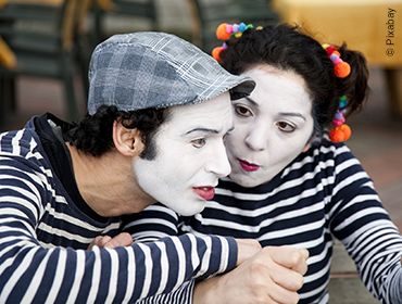 Zwei Personen in pantomimischer Darstellung. Der Mann sieht fragend nach vorne und die Frau blickt ihn gezielt mit einer Fischmund-ähnlichen Mimik an.